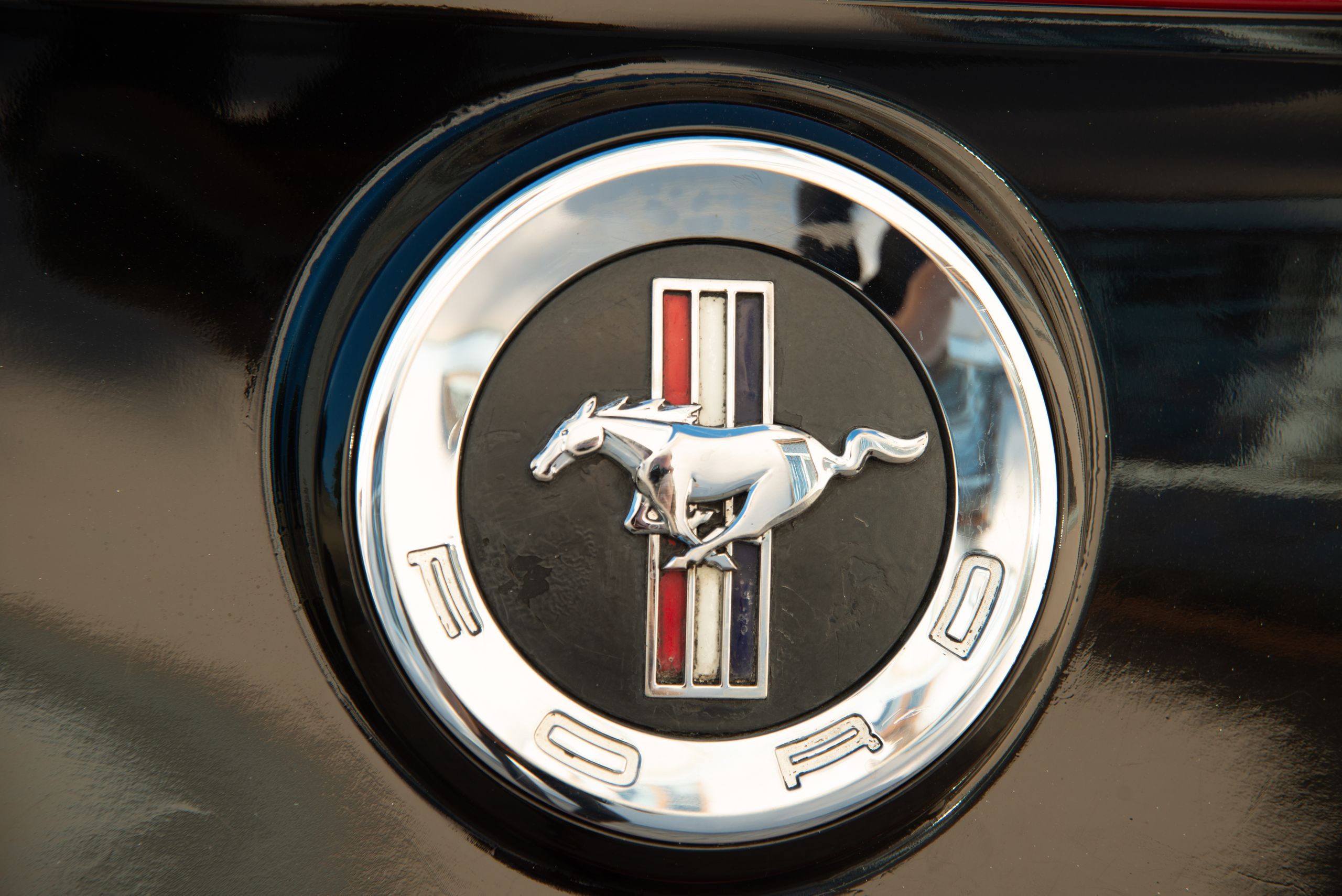 Detailed close-up of Ford Mustang emblem on a vehicle's black surface, symbolizing speed.